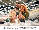 Small photo of Red-haired sweet woman with her boyfriend chooses new smartphone in store of household appliances, electronics and gadgets.