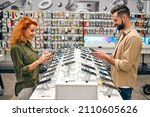 Red-haired sweet woman with her boyfriend chooses new smartphone in store of household appliances, electronics and gadgets.