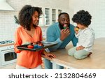 Small photo of An African American family with their little daughter with curly fluffy hair made cupcakes together in the kitchen. Mom brought a baking sheet with ready-made muffins and gives the family a try.