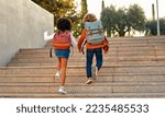 Small photo of Happy smart kids with school bags rush to the lessons to school running up the stairs. Back to school. An African-American schoolgirl and her classmate walk down the street after school.