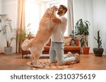 Handsome bearded man playing and training his labrador dog while sitting on the floor in the living room at home, having fun together.