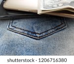 Cash money and smart phone on blue jeans background implying a young small business owner who start online business or e-commerce to make money.