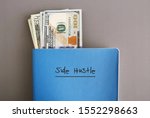 Cash dollar money in a blue notebook with text written on cover SIDE HUSTLE, on grey background, concept of making more money from side job with writing or freelance job