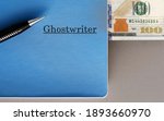 Small photo of Cash money, pen, blue notebook with text typed GhostWriter, on copy space grey background, concept of income from being ghostwriter (talented writer who hired to work and credited client as writer)
