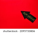 Small photo of Black arrow on copy space red background with handwritten text AIM HIGH, means to be ambitious or to direct efforts or strive to be better, set larger or harder goals to achieve