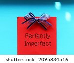Red note with blue ribbon on blue background with handwritten text PERFECTLY  IMPERFECT, concept of accept yourself no matter what, with all flaws, imperfections make life interesting and help us grow