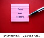 Small photo of On red background, pen writing on note pad KNOW YOUR TRIGGERS, learning to know experience of having emotional reaction to a disturbing topic in the media or social setting and empower to cope with it