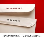 Small photo of Office envelopes with handwritten text OVERWORKED and UNDERPAID, means employees or workers who work too hard or too long but get paid less than what they deserve