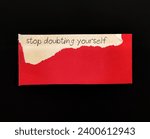 Small photo of Torn red note on black background with handwriting STOP DOUBTING YOURSELF, concept of self-doubt, lack of confidence mindset that hold back from succeeding leads to imposter syndrome or self sabotage