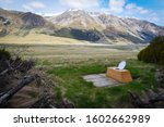 Outdoor toilet with an open toilet seat in the middle of wilderness located in a valley surrounded with many mountains and with an epic view in New Zealand