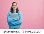 Cute looking girl, student, woman and female in studio holding her laptop or computer in arms beside copy space. Pink and blue colorful portrait on pink background. 