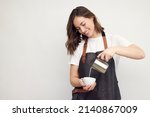 Professional smiling barista woman in studio serving coffee, pour milk from a jug in a coffee cup. Café latte. Isolated on white background.