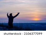 Small photo of Prayer. Repentance. Silhouetted men on a background of blue sky and sunset. Kneeling Prayer to God. Glorification. Praising God. Jesus is risen. Man with raised hands