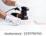 Small photo of Eccentric grinding machine in hands. Power tool. On a white background. The master of wood blocks in gloves grinds