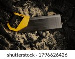 Small photo of Backsaw with yellow handle on black background and sawdust.