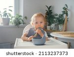 Small photo of A baby making its first attempts to eat by itself. An infant sitting in highchair in dinning room, holding a spoon and eating