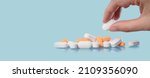 Small photo of Medical background. Hand holds one of many capsule tablets or pills on blue table. Close up. Healthcare pharmacy and medicine concept with copy space Painkillers or prescription drugs consumption