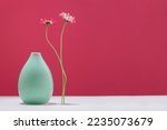 Small photo of Two daisy spring flowers near a tiny green vase on table. Misplaced eccentric. Fragile. assumptions. Unordinary. Viva magenta background with copy space. Blooming flowers. Greeting card. Border banner