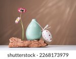 Small photo of Happy Easter egg. Two daisy spring flowers near a tiny green vase on a rock on table. Misplaced eccentric. Fragile. Brown background with copy space. Blooming flowers. Greeting card. sunlight