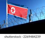 The North Korean flag hangs in the cloudy sky outside the prison's barbed wire. waving in the sky