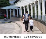 Mother or domestic helper hold hand of son or kid of kindergarten or primary school student, carrying school bag walk to or from school in  street in Hong Kong on sunny day