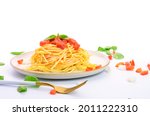 Spaghetti or pasta with tomato sauce and fresh green basil on a white plate with tomato isolated fork on a white background - top view
