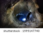 Speleologist descend by the rope in the deep vertical cave tunnel.  Cave man hanging over abyss. View from the top og the tunnel. Silhouette image. Karst cave. Caucasian mountains. Abkhazia.