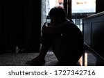 Small photo of Depressed Asian man sitting on the floor hugging knees and looking away distraught with sadness. Loneliness sad man living alone and listening music from headphone. Mental health and drug abuse.