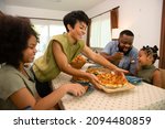 African mixed race family parents and two little daughter eating fried chicken and pizza for dinner together. Father and mother and cute child girl kid enjoy eating and sharing a meal together at home