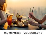 Young Asian woman friends celebrating dinner party meeting at skyscraper rooftop restaurant bar in metropolis at summer sunset. Beautiful girl enjoy outdoor lifestyle together on holiday vacation.