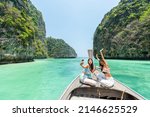 Small photo of Young Asian woman friends using mobile phone taking selfie together while travel on boat passing island beach lagoon in sunny day. Happy female enjoy and fun outdoor lifestyle on summer vacation trip