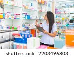 Small photo of Medical pharmacy and healthcare drug providers concept. Attractive Indian woman pharmacist working checking stock of medical product, drugs, medicine and supplements on shelf in modern drugstore.
