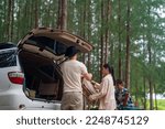 Small photo of Group of Asian people friends enjoy outdoor lifestyle road trip and camping together on summer holiday travel vacation. Man and woman taking off camping supplies from car trunk at natural park.