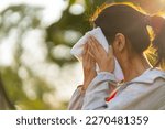 Asian woman in sportswear wiping sweat on her face with towel during jogging exercise at public park at summer sunset. Healthy girl enjoy outdoor lifestyle sport training workout running in the city.