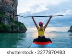 Asian mature woman sitting on paddle board and rowing in the ocean at tropical island at sunset. Wellness woman enjoy outdoor lifestyle and water sports surfing and paddle boarding on summer vacation.