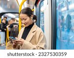 Asian woman using mobile phone and listening to the music on earphones during travel on train in the city. Attractive girl enjoy urban lifestyle with using digital gadget device and online network.