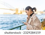 Asian woman using mobile phone during travel on ferry boat crossing harbor in Sydney, Australia. Attractive girl enjoy outdoor lifestyle travel in the city with gadget device on holiday vacation.