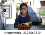Small photo of Dehradun, Uttarakhand, India 12-09-2023: Cute Indian girl standing and holding Prasad (Gracious gift) in plate on Kanjika Ritual or Kanjak during the Navratri festival.