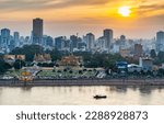 Small photo of Rooftop view,looking across to the Riverside area of Cambodia's capital city.Sunset over Royal Palace and high rise buildings beyond, as a small boat drifts by towards the Mekong river.