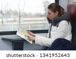 Small photo of Adult young woman in warm sacual clothes travelling and looking for a route on the map how to get somewhere in the train
