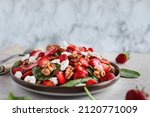 Plate of homemade fresh salad of baby spinach leaves, sliced strawberries, walnuts, feta cheese, and a light vinaigrette dressing. Selective focus with extreme shallow depth of field.