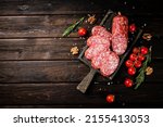 Pieces of salami sausage on a cutting board with cherry tomatoes and rosemary. On a wooden background. High quality photo
