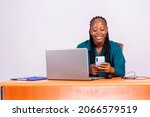 smiling young black African woman using her smart phone and modern laptop , reading text message, sitting at desk with gadgets, shopping online using social media working at home office Business