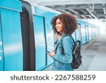 Happy young tourist African American woman with backpack and holding smartphone while at the train station and the train is arriving., Enjoying travel concept