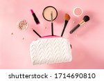 Small photo of Professional makeup, flying out of a bag, on a pink background. Lipstick, brushes, powder compact, a creative beauty design