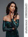 Small photo of Stunning brunette with a voluminous hairstyle in a graceful green evening gown against a gray backdrop