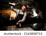 Small photo of view on cocktail making process where professional male bartender skillfully pours a cocktail from one shaker cup to another at bar