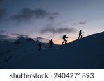 Silhouettes of four skiers on the highest point of the mountain against the background of the mountain peaks in the fog and the red sky