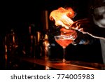 Barman`s hands making a fresh alcoholic cocktail with a smoky note on the dark bar counter