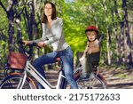 Mother with little blond boy on e-bicycle on backseat on the alley in the park